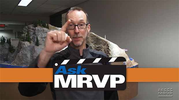 David Popp standing in front of an N scale model railroad and holding up his pointer finger.