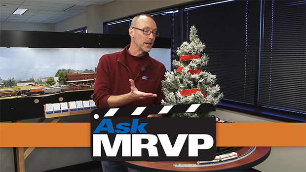 David Popp standing next to a table that has a small Christmas tree and trains set up to run around it.