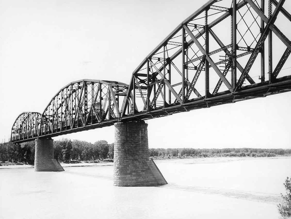 Steam-powered passenger train on large truss bridge over water