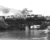 Two diesel locomotives on deck truss bridge over water