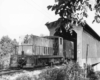 Diesel switcher locomotive exits wooden covered bridge with train