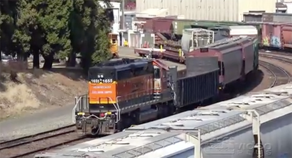 An orange-painted locomotive on a freight train on a curve on a well sunlit day.