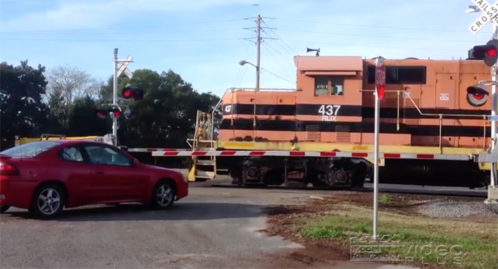 An orange-and-black locomotive moves through a grade crossing with the crossing gates down.