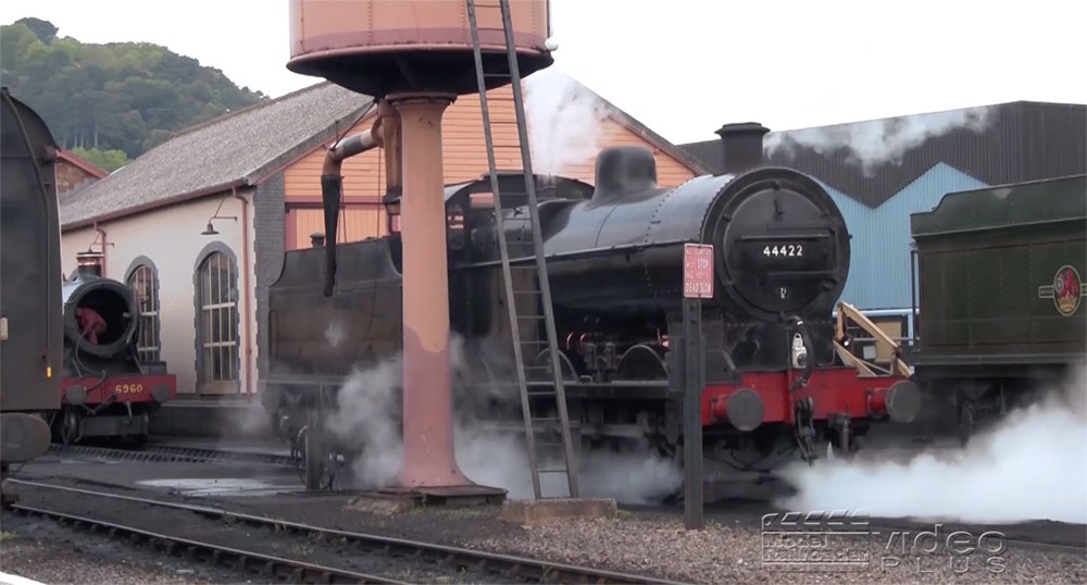 A black-painted steam locomotive releases steam in a UK rail yard.