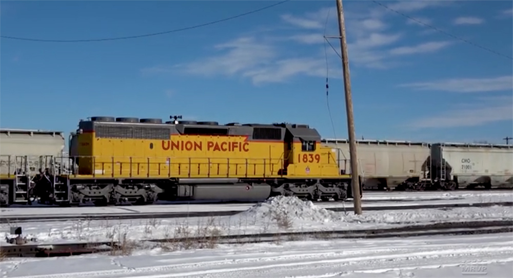 A yellow-painted Union Pacific locomotive stands alone in a yard in snow under mostly clear skies.