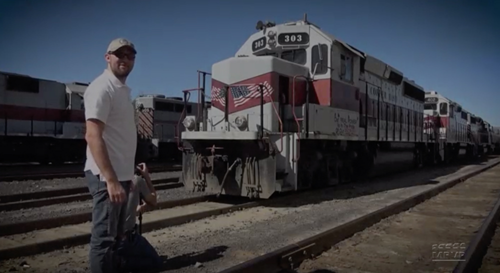 Man stand in front of a diesel locomotive in a rail yard.