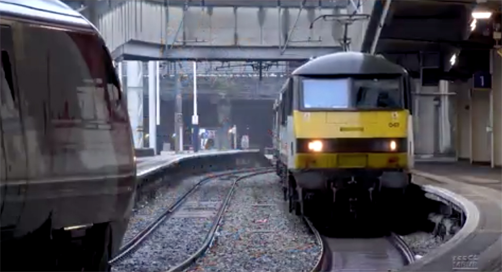 A UK locomotive with a wide windshield and yellow paint face the camera head on at a station platform.