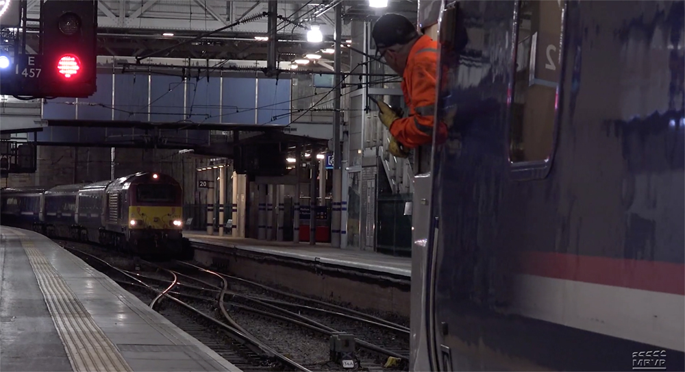 UK-style passenger trains near a station platform, one paused in front of a "Stop" signal.