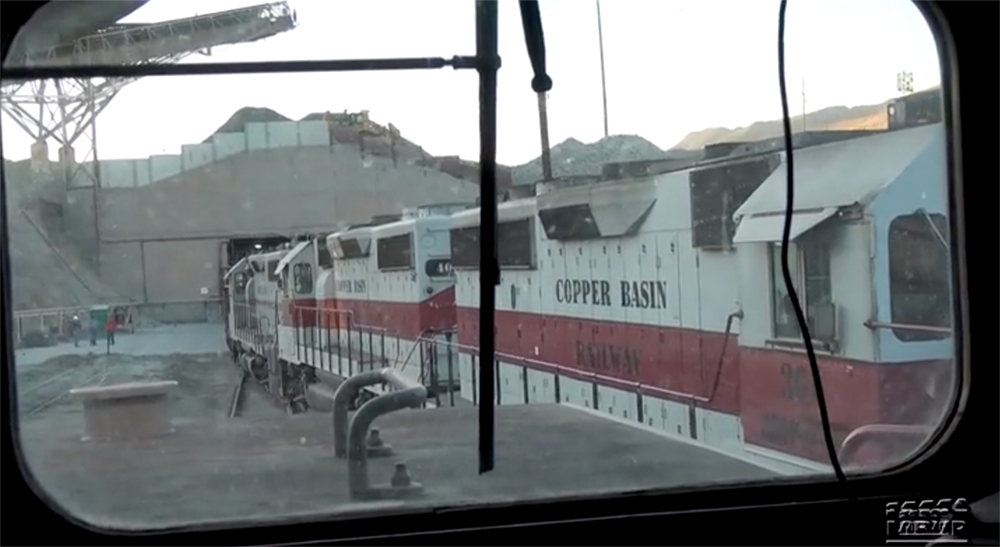 View from inside a locomotive cab at gray with red-stripe diesel locomotives in a yard.
