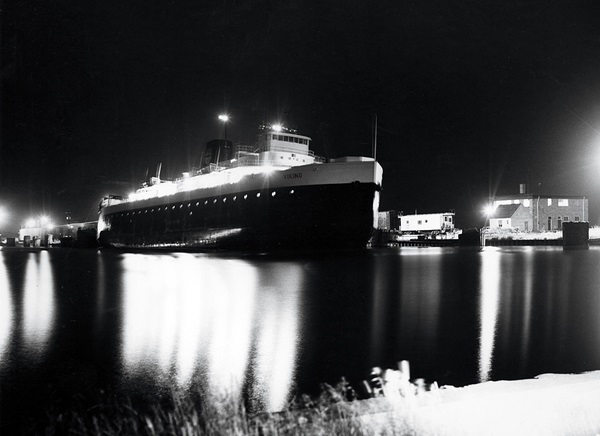 A well lit ship docked at night.