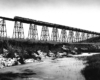 Diesel locomotives pull a long freight train over a high bridge.
