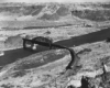 Wide scene of high-desert and mountains with a cab unit led train crossing a river.