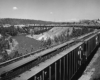 Covered hopper train on a mountain plateau crossing a bridge and river.