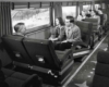 Several people in cloth cushioned bench-style coach seats looking out a passenger coach on a snowy scene.