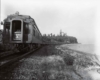 Passenger train rounding a curve along a shoreline as viewed from behind the train.