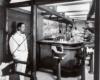 People seated at a bar and a white-suited waiter standing by.