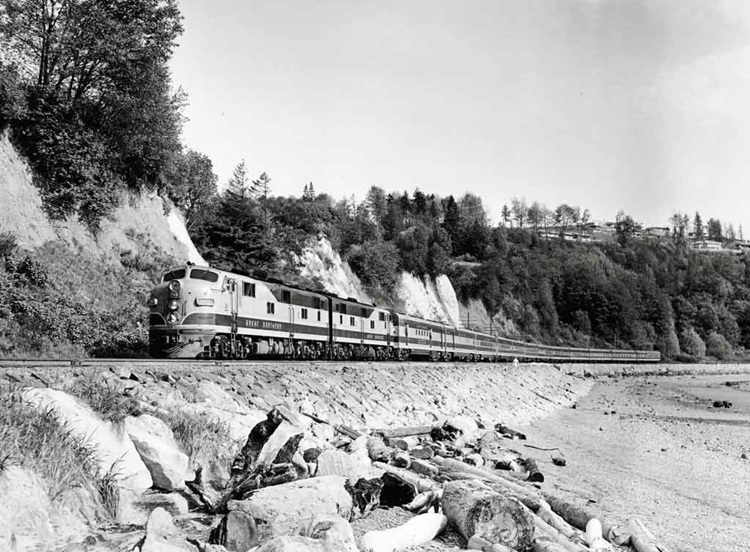 Diesel locomotive-led passenger train seen near a sandy beach.