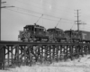 Three freight motors haul a freight train over a trestle.