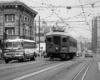 An interurban car operates in the middle of a busy downtown street.