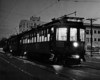 Three lighted streetcars operating in darkness on a city street.