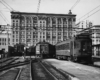 Passenger train terminal in an early 20th century city scene filled with streetcars or interurban cars.
