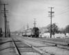 Two electric interurban cars in the middle ground on a straight stretch of four-track main line.