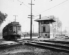 Streetcar or electric interurban car about to cross a double-diamond overlooked by an interlocking tower.