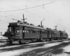Three electric interurban or streetcars paused on a multi-track main line.