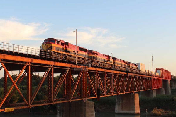 Red, black, and yello locomotives pulling train across bridge