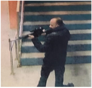 Grainy image of balding man holding and appearing to aim a long gun in front of steps.