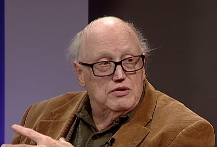 Balding caucasian man wearing eyeglasses and brown coat.