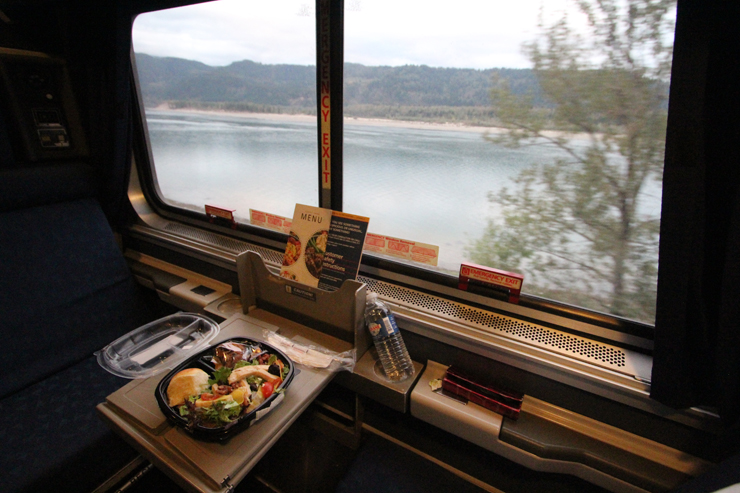 A meal on a small table in a passenger car overlooking a river.