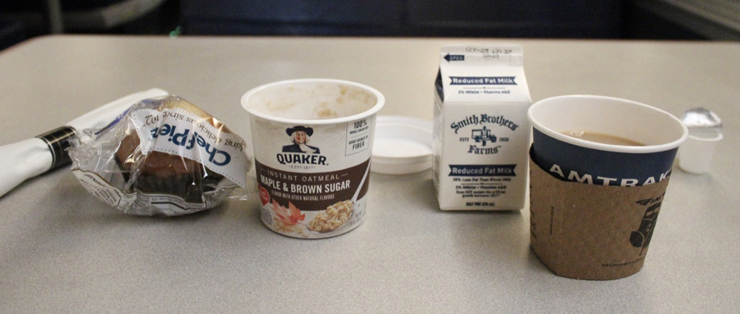 From left: packaged muffin, oatmeal in a paper cup, small milk carton, what appears to be coffee in a paper cup.