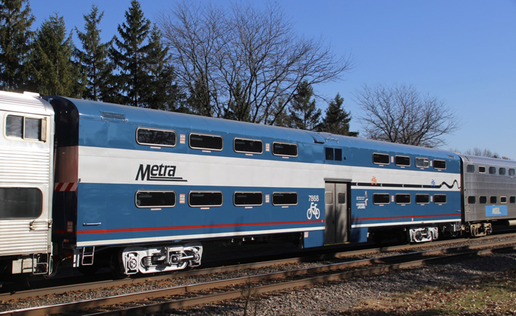 A blue painted bi-level passenger car in a passenger train under cloudless skies.