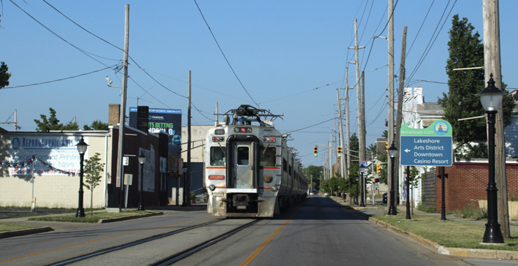 A silver passenger train operates in the middle of a street.