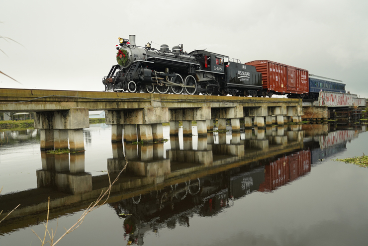 Steam locomotive pulling train over water on a pile causeway.