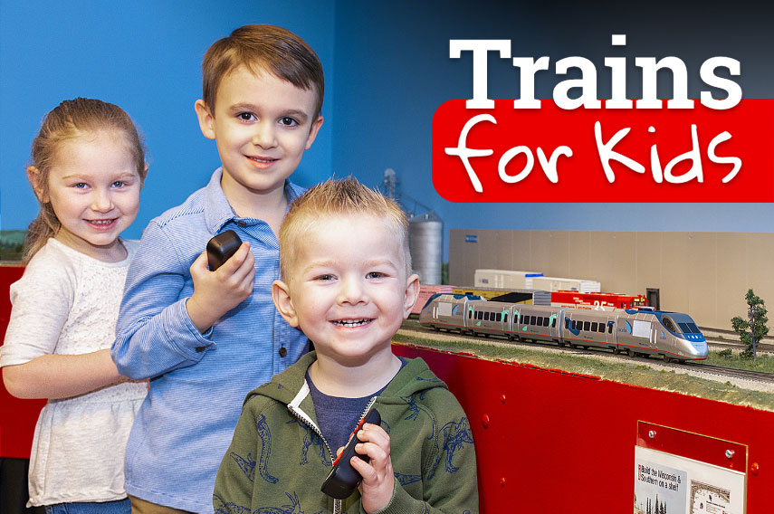 Two young boys and a girl holding controllers in front of a HO layout