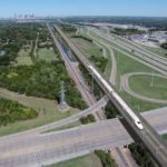 Birds eye view of a rail line passing over a complex highway interchange.