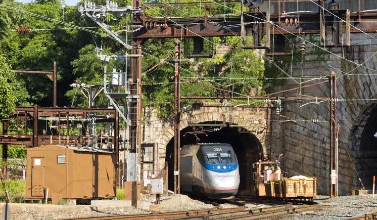 An Amtrak Acela train exits a tunnel in a mountainside.