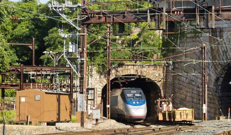 An Amtrak Acela train exits a tunnel in a mountainside. Amtrak awards two contract for Frederick Douglass Tunnel project.