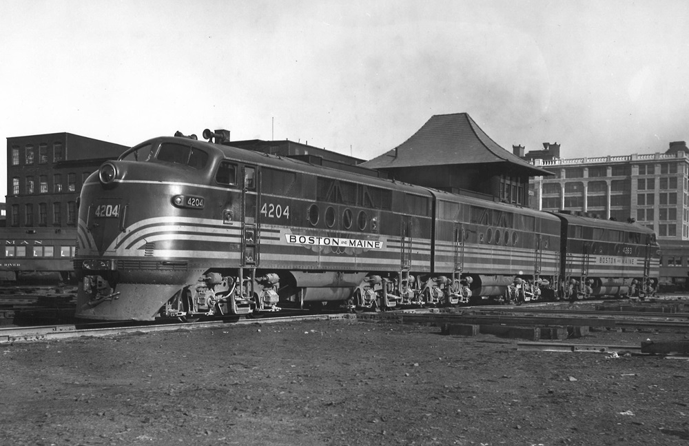 Three cab unit style diesel locomotives pause in a freight yard.