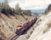 Four locomotives pull a freight train uphill.