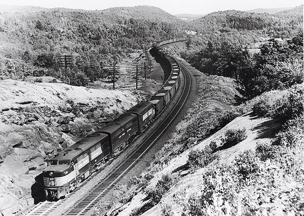 Three streamlined diesel locomotives with freight train in mountains.