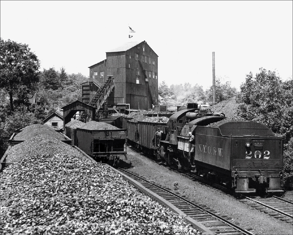 Coal hoppers being switched by a camelback steam locomotive and loaded with coal.