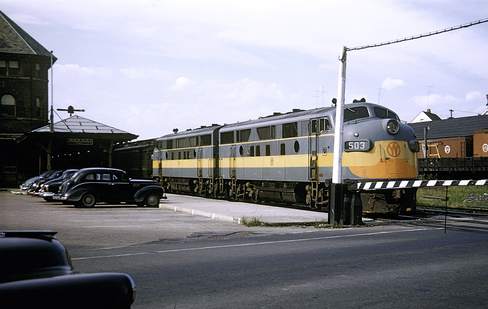 Two locomotives with a passenger train pause at a station.