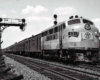 One cab unit diesel locomotive leads a passenger train over a multi-track mainline.