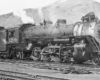 Side view of a 2-8-2 steam locomotive at the foot of an arid mountain.