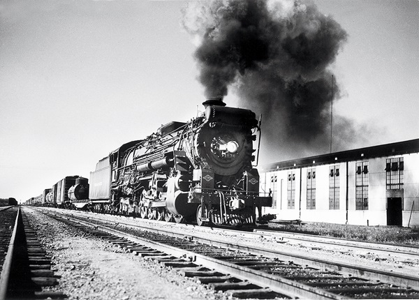 Steam locomotive hauling freight train emitting large plume of smoke.