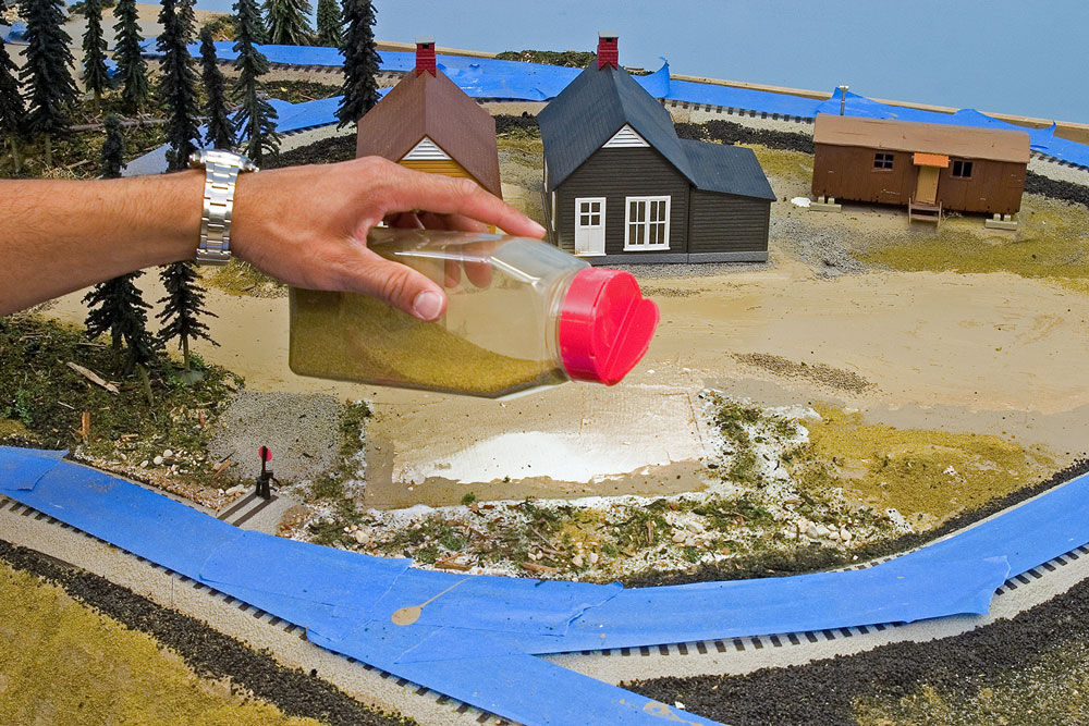 Hand sprinkling green ground foam on model railroad layout.