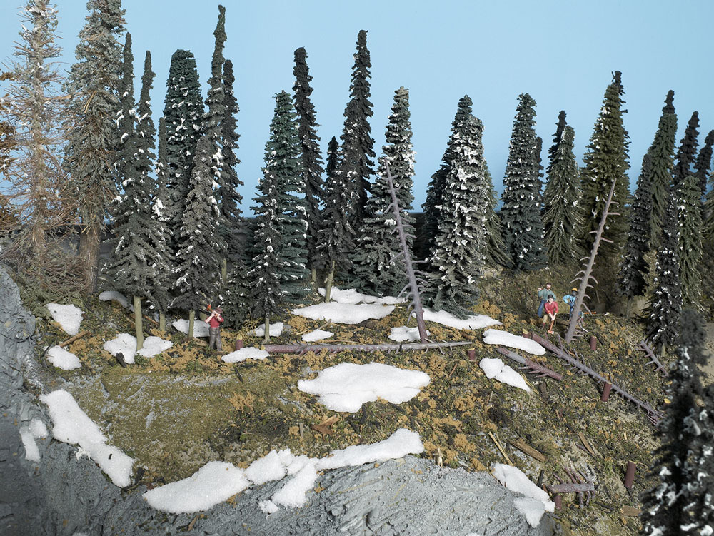 Model scene featuring lumberjack figures, coniferous trees, and Styrofoam resembling melting snow.